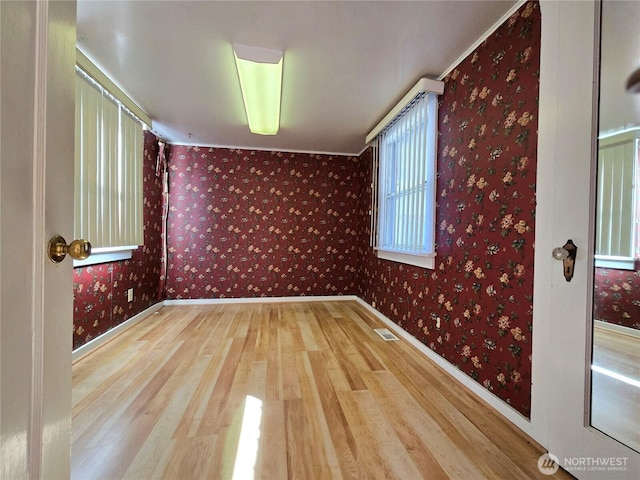 unfurnished room with baseboards, wood finished floors, visible vents, and wallpapered walls