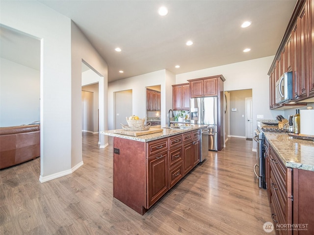 kitchen with light stone counters, recessed lighting, wood finished floors, a sink, and appliances with stainless steel finishes