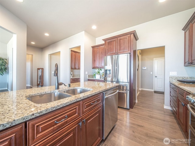 kitchen featuring light stone countertops, light wood-style flooring, appliances with stainless steel finishes, and a sink