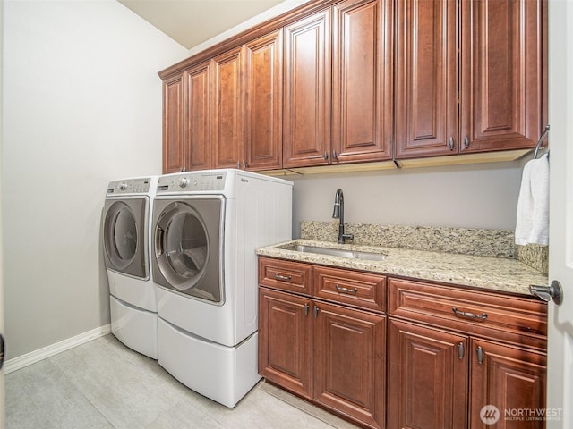 clothes washing area featuring cabinet space, a sink, washer and clothes dryer, and baseboards