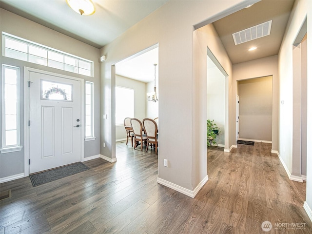 foyer with baseboards, visible vents, dark wood finished floors, and a notable chandelier