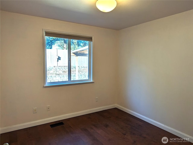 spare room featuring dark wood-style floors, visible vents, and baseboards