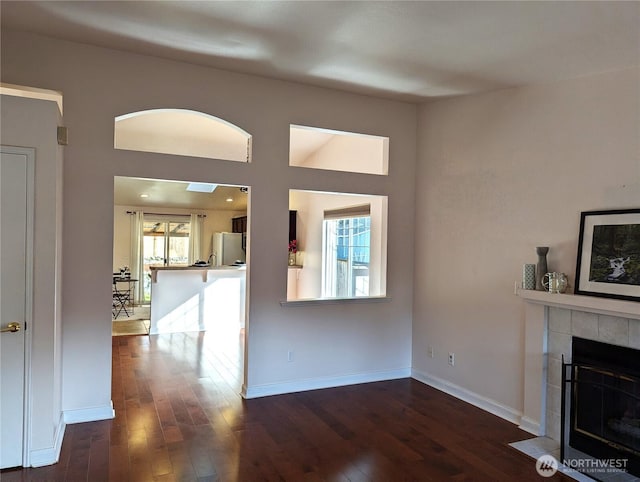 unfurnished living room featuring dark wood-type flooring, a fireplace, and baseboards