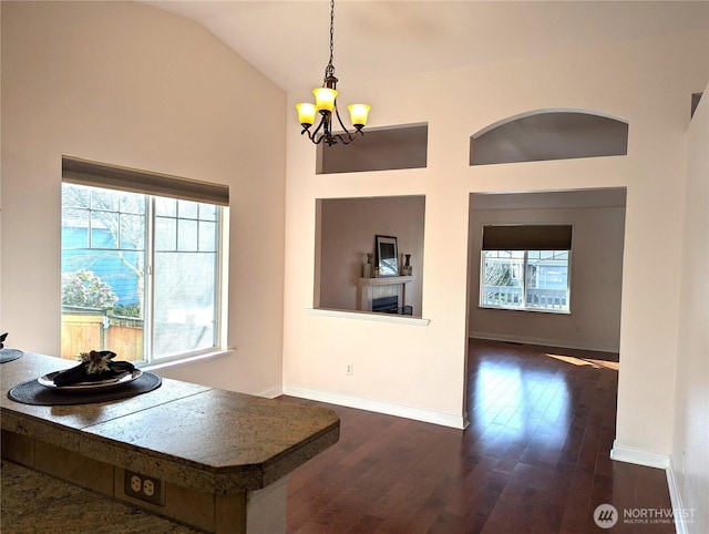 kitchen with hanging light fixtures, an inviting chandelier, dark wood-type flooring, high vaulted ceiling, and baseboards