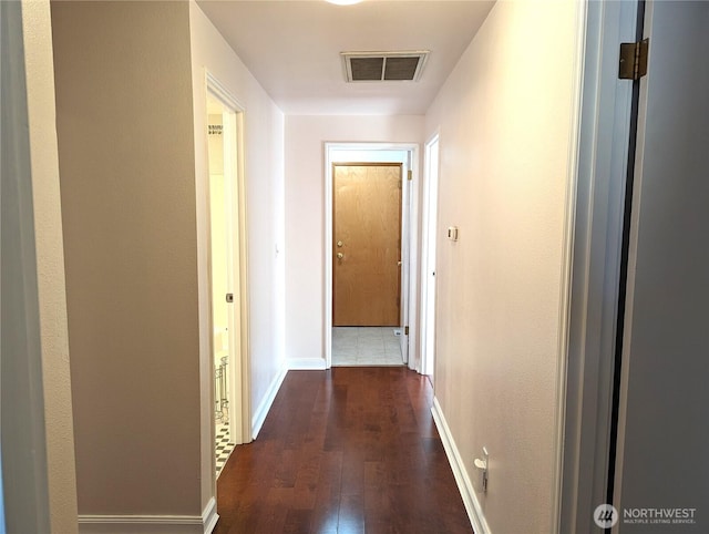 hallway with dark wood-type flooring, visible vents, and baseboards