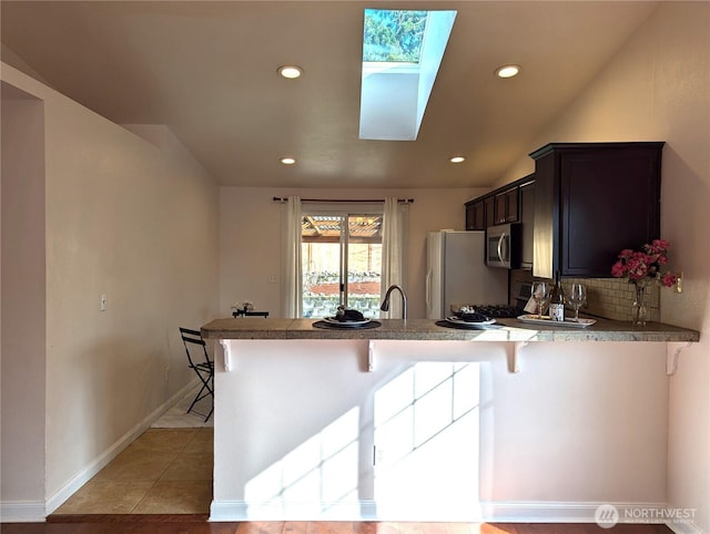 kitchen with stainless steel microwave, decorative backsplash, freestanding refrigerator, a peninsula, and a kitchen bar