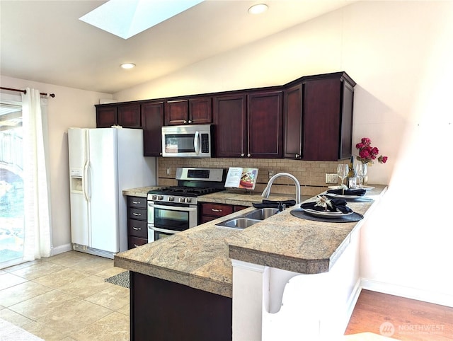 kitchen featuring vaulted ceiling with skylight, appliances with stainless steel finishes, a peninsula, a sink, and backsplash