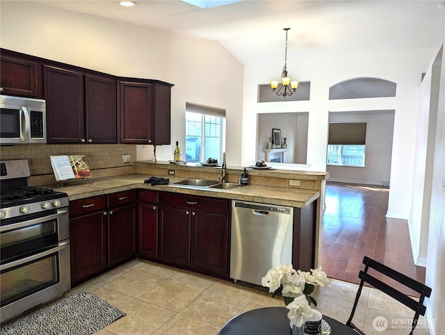 kitchen featuring decorative backsplash, a peninsula, hanging light fixtures, stainless steel appliances, and a sink