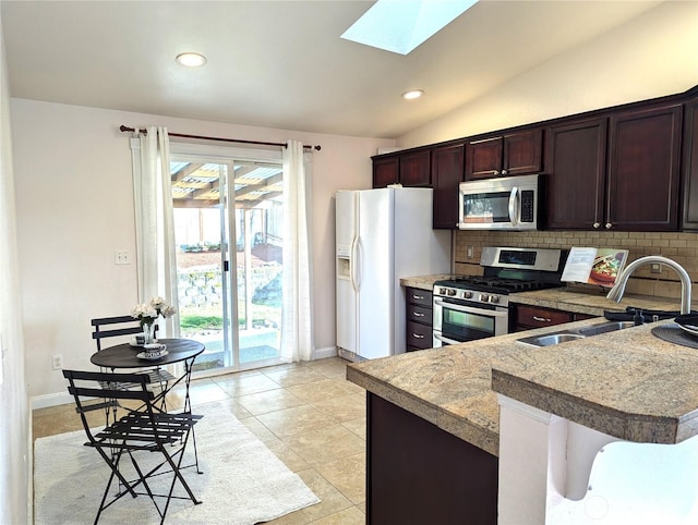 kitchen featuring stainless steel appliances, vaulted ceiling with skylight, a sink, and tasteful backsplash