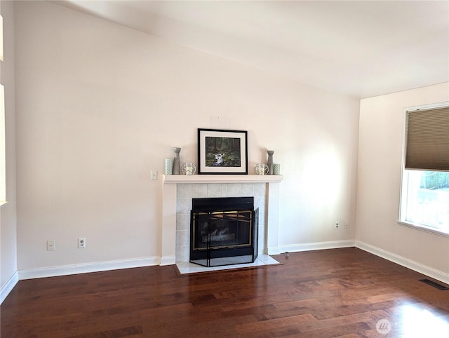 unfurnished living room with baseboards, a tiled fireplace, visible vents, and wood finished floors