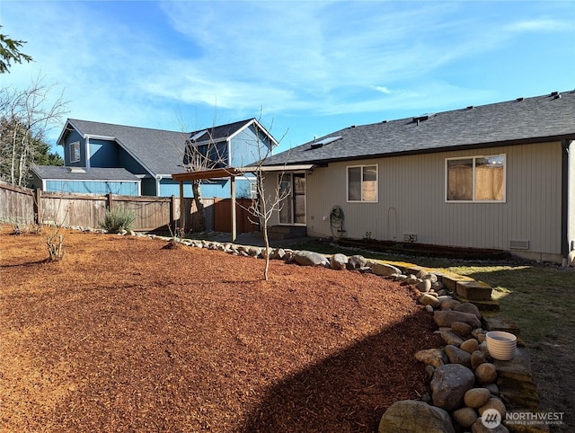 rear view of house with a shingled roof, crawl space, and fence