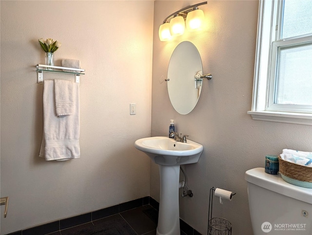 half bathroom featuring toilet, a sink, a wealth of natural light, and tile patterned floors