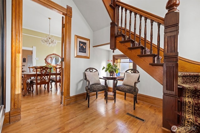 sitting room with high vaulted ceiling, wood finished floors, visible vents, stairs, and an inviting chandelier