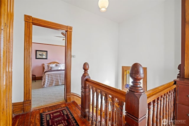 hall featuring baseboards, hardwood / wood-style floors, and an upstairs landing