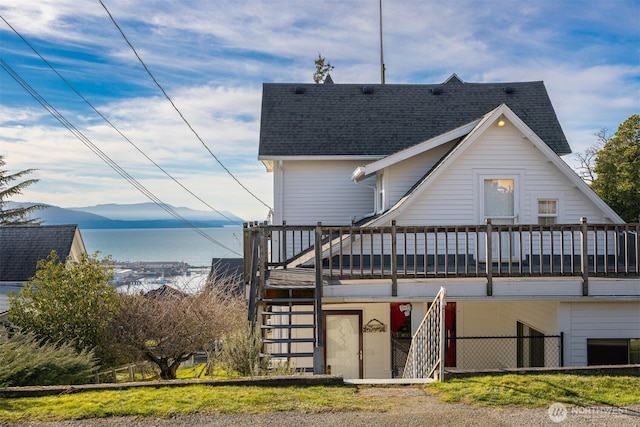 rear view of property with a deck with mountain view, stairway, and roof with shingles