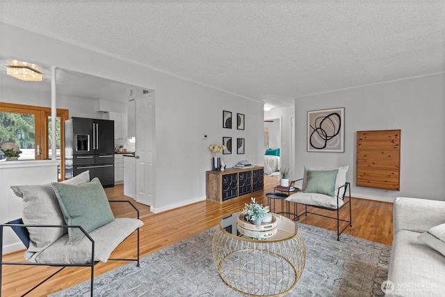 living area with baseboards, a textured ceiling, and light wood finished floors