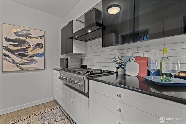 kitchen with appliances with stainless steel finishes, decorative backsplash, wall chimney range hood, and light wood finished floors