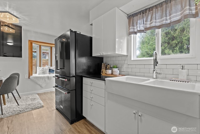 kitchen featuring tasteful backsplash, black fridge, a wealth of natural light, and white cabinetry