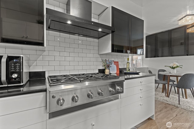 kitchen with dark countertops, stainless steel gas stovetop, backsplash, wall chimney range hood, and light wood-type flooring