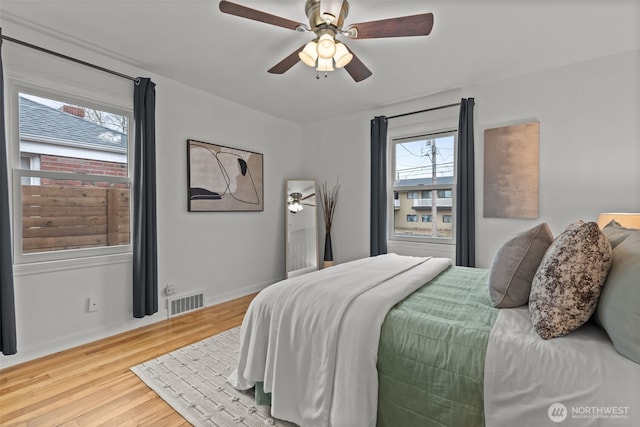 bedroom featuring baseboards, wood finished floors, visible vents, and a ceiling fan