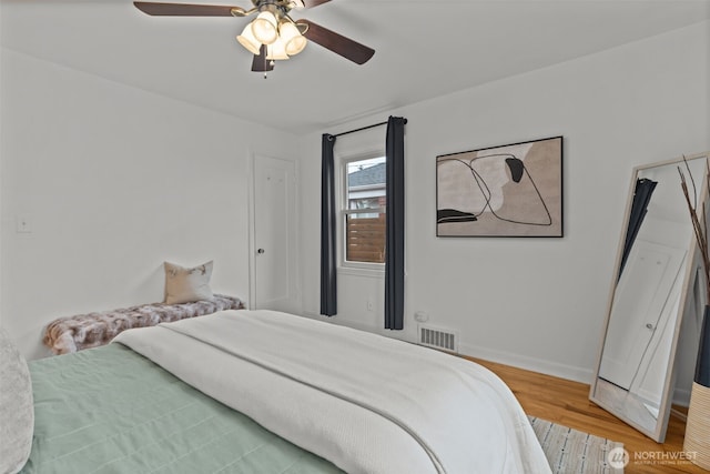 bedroom with a ceiling fan, wood finished floors, visible vents, and baseboards