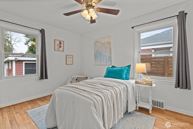 bedroom with ceiling fan, wood finished floors, visible vents, and baseboards