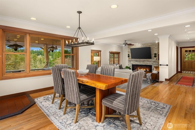 dining area with baseboards, crown molding, a stone fireplace, light wood-style floors, and recessed lighting