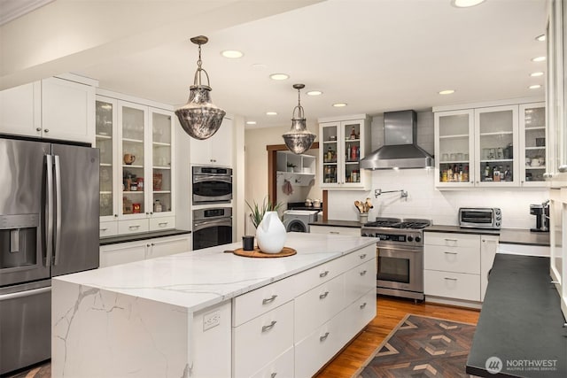 kitchen featuring stainless steel appliances, a center island, white cabinetry, decorative backsplash, and wall chimney exhaust hood