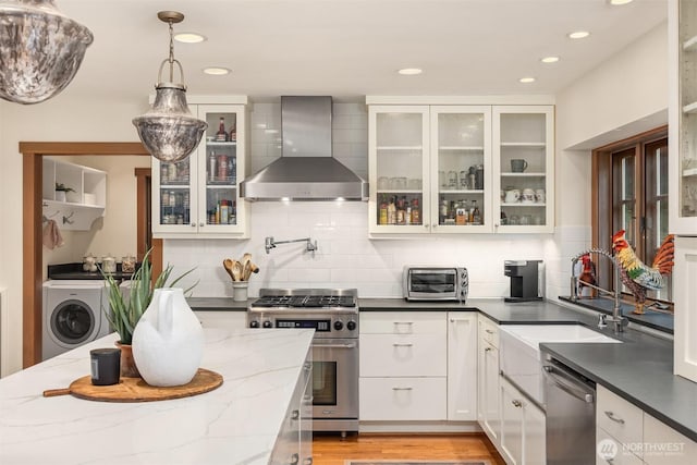 kitchen with washer / dryer, wall chimney exhaust hood, appliances with stainless steel finishes, white cabinetry, and a sink