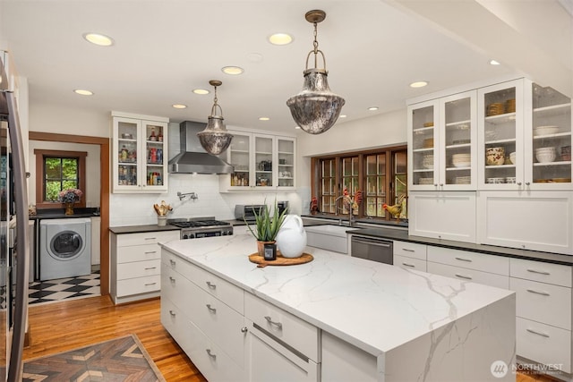 kitchen with washer / dryer, dishwasher, a kitchen island, stove, and wall chimney range hood