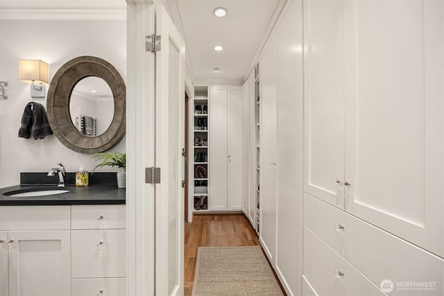 corridor with ornamental molding, recessed lighting, a sink, and light wood-style floors