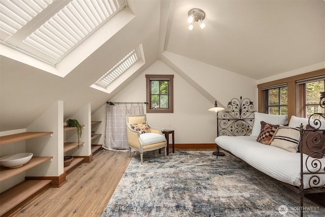 sitting room featuring light wood-type flooring, vaulted ceiling with skylight, and baseboards