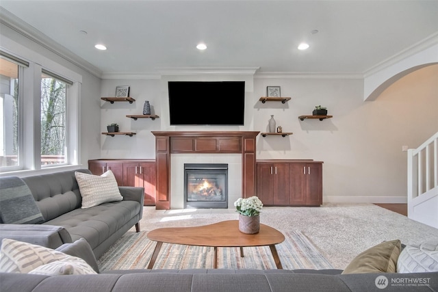 carpeted living room featuring baseboards, arched walkways, crown molding, a fireplace, and recessed lighting