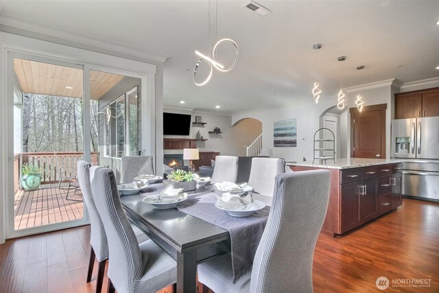 dining room with a warm lit fireplace, visible vents, dark wood-style floors, and arched walkways