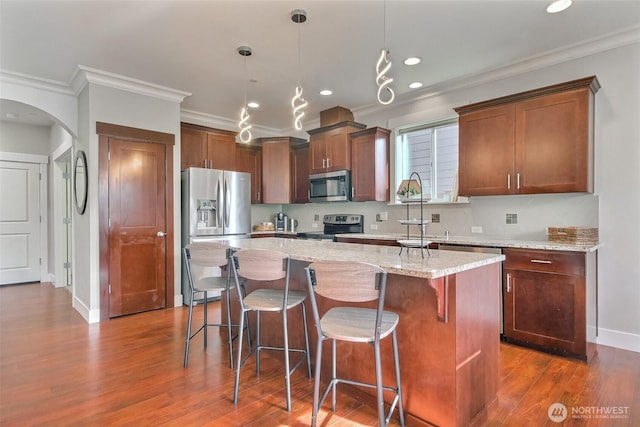 kitchen featuring arched walkways, stainless steel appliances, a sink, ornamental molding, and a center island