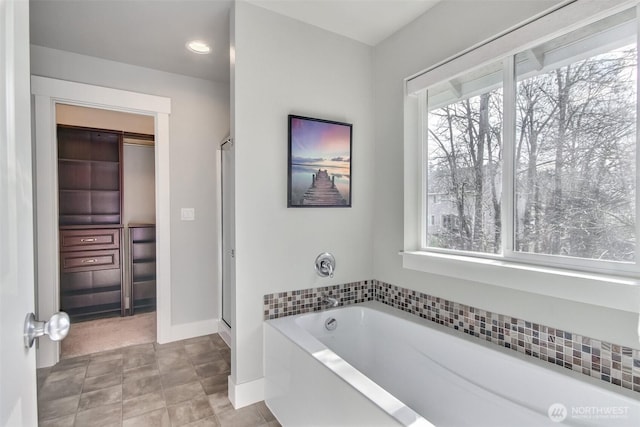 bathroom featuring a garden tub, a shower stall, and baseboards