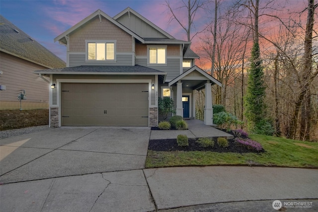 craftsman-style home featuring a garage, a shingled roof, driveway, stone siding, and board and batten siding