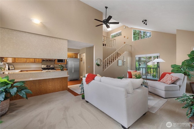 living room with stairs, high vaulted ceiling, a ceiling fan, and light carpet