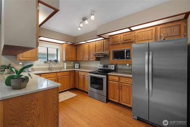 kitchen with brown cabinetry, a sink, stainless steel appliances, light wood-style floors, and under cabinet range hood