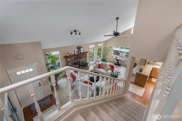 stairs featuring a stone fireplace, ceiling fan, wood finished floors, and high vaulted ceiling