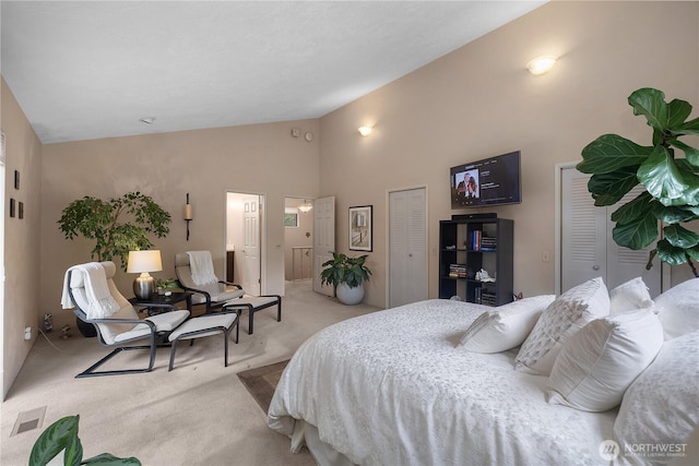 carpeted bedroom featuring visible vents, two closets, and high vaulted ceiling