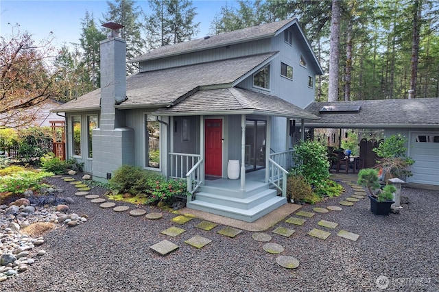 view of front facade with a garage, a chimney, and a shingled roof