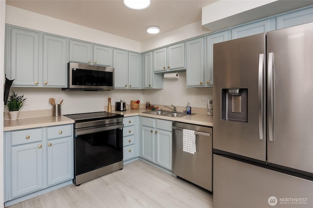 kitchen with light wood-type flooring, stainless steel appliances, a sink, and light countertops