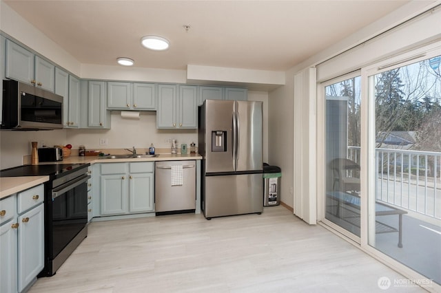 kitchen featuring stainless steel appliances, light countertops, gray cabinetry, a sink, and light wood-type flooring