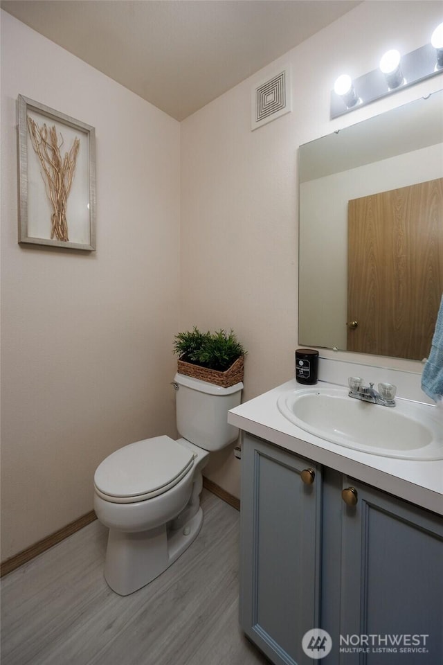 bathroom with toilet, wood finished floors, vanity, visible vents, and baseboards