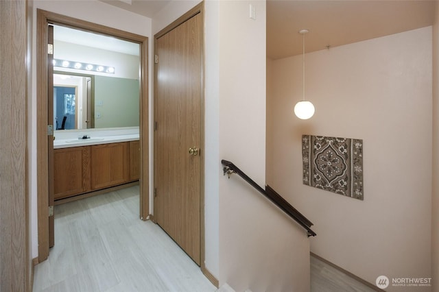 hallway featuring light wood-style floors, a sink, and an upstairs landing