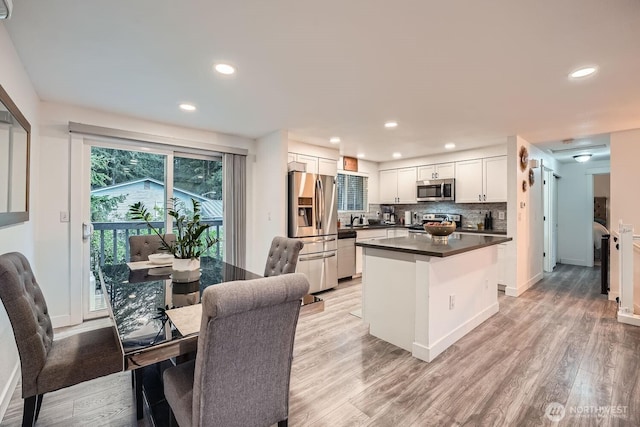 kitchen featuring dark countertops, tasteful backsplash, light wood finished floors, appliances with stainless steel finishes, and white cabinetry