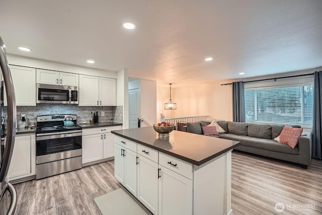 kitchen featuring stainless steel appliances, tasteful backsplash, dark countertops, and open floor plan