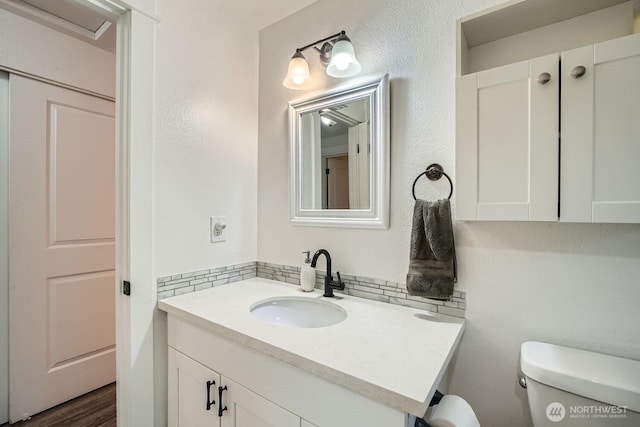 half bath featuring toilet, wood finished floors, decorative backsplash, vanity, and a textured wall
