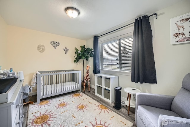 bedroom with baseboards, a nursery area, and wood finished floors